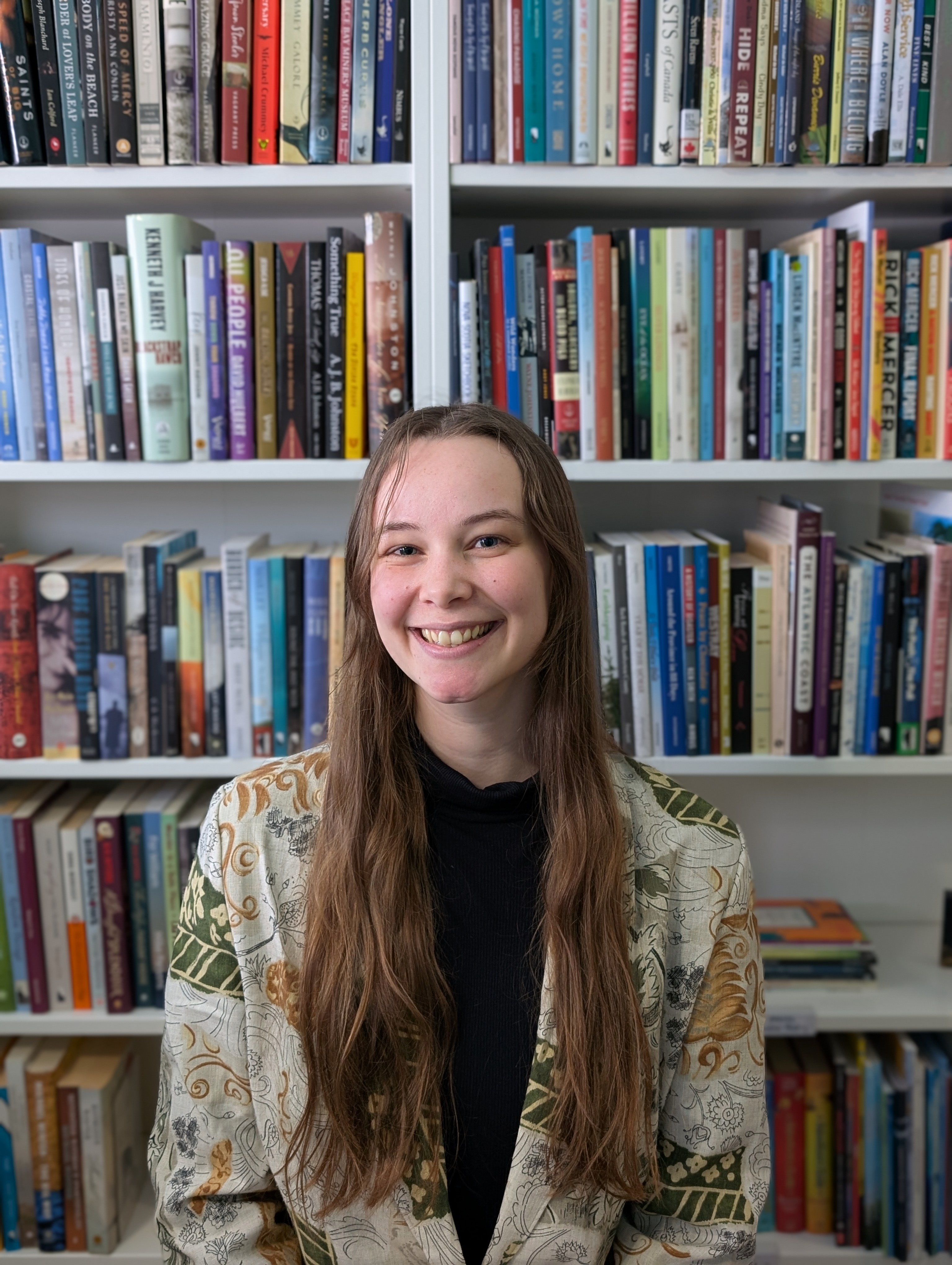 Picture of woman with long hair in a linen blazer posing in front of a bookshself.